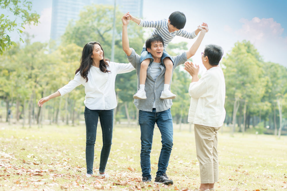 Family of four enjoying a day out in a park with trees and clear sky.