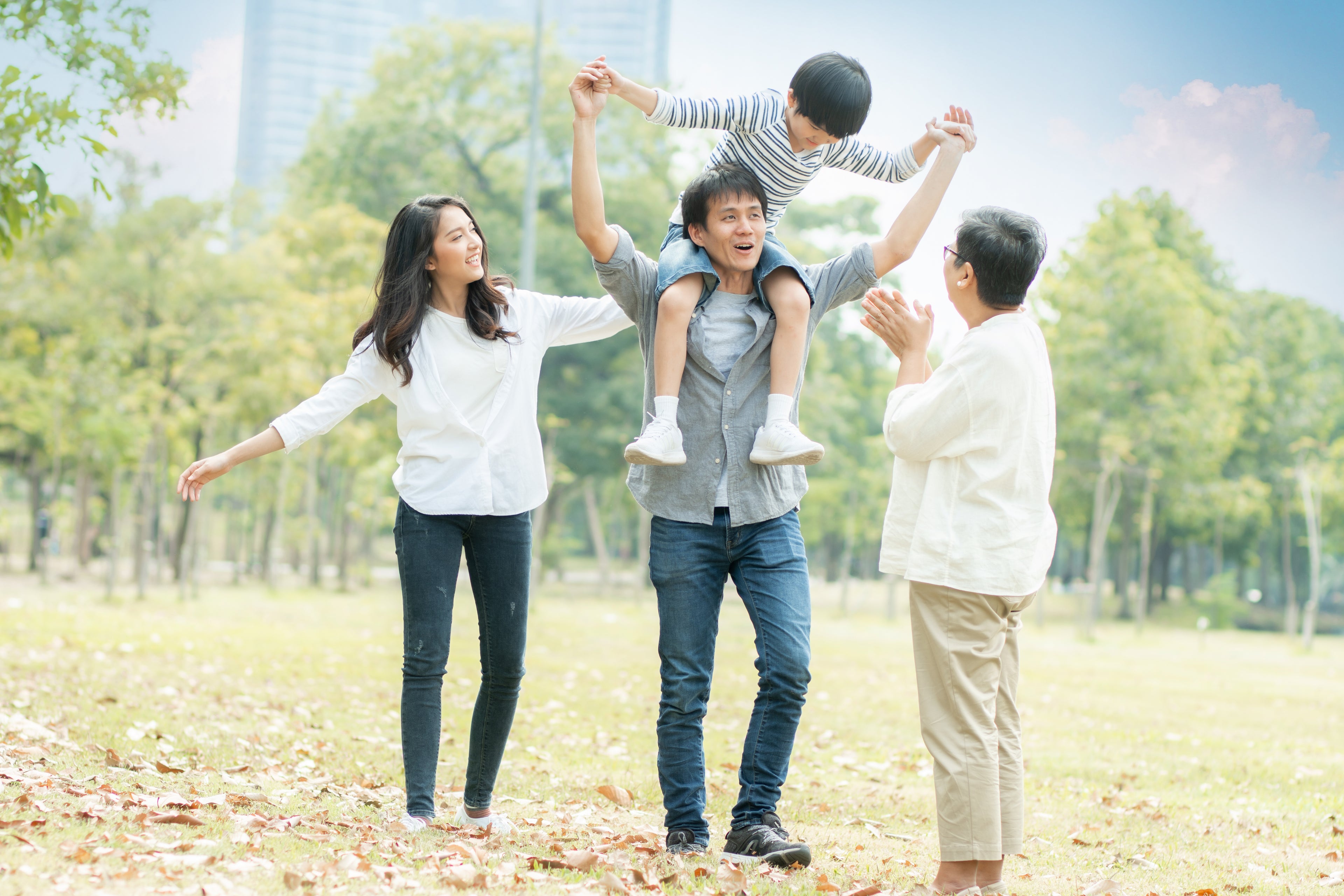 Family of four enjoying a day out in a park with trees and clear sky.